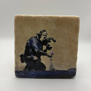 Banksy's artwork featuring a cameraman and flower printed on square travertine stone coaster