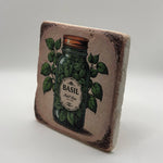 Vintage-style illustration of basil leaves printed on square travertine stone coaster