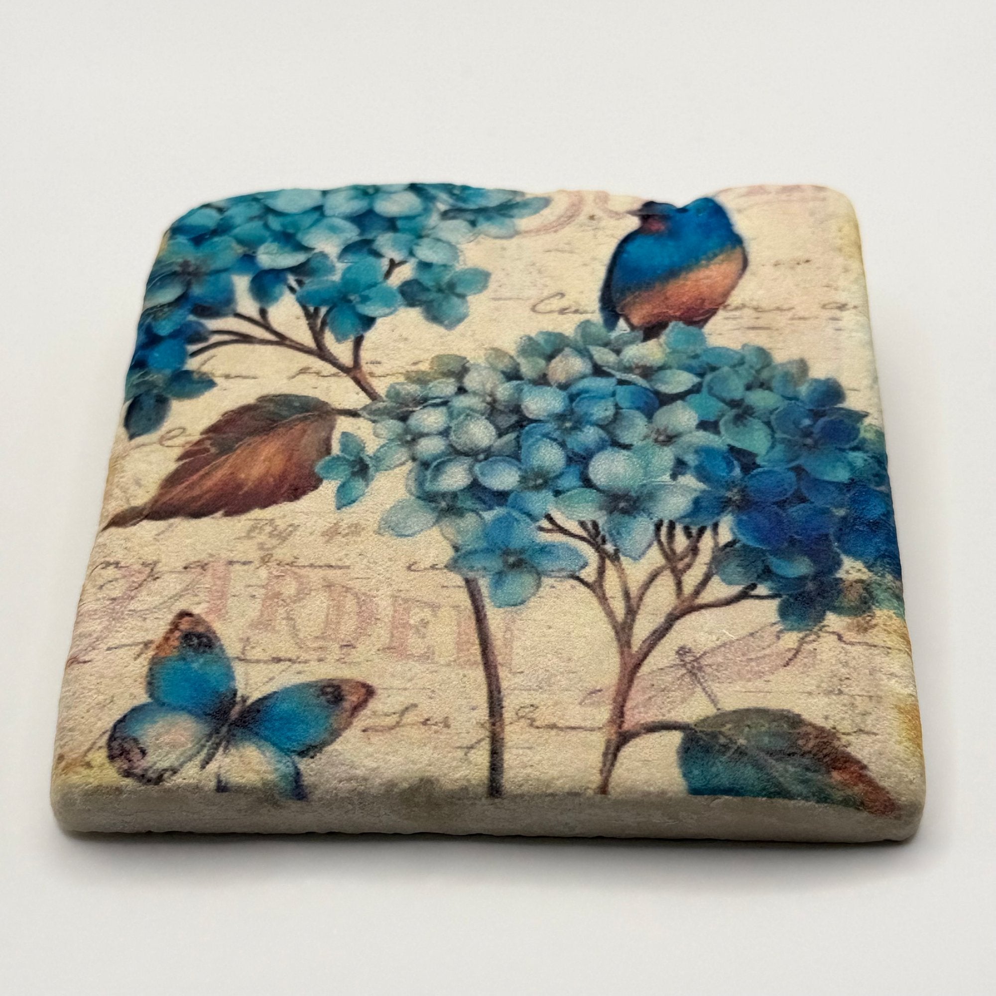Illustrated bird, flower, and butterfly artwork printed on square travertine stone coaster