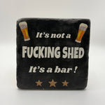Funny quote 'It's Not a Fucking Shed It's a Bar' printed on square travertine stone coaster