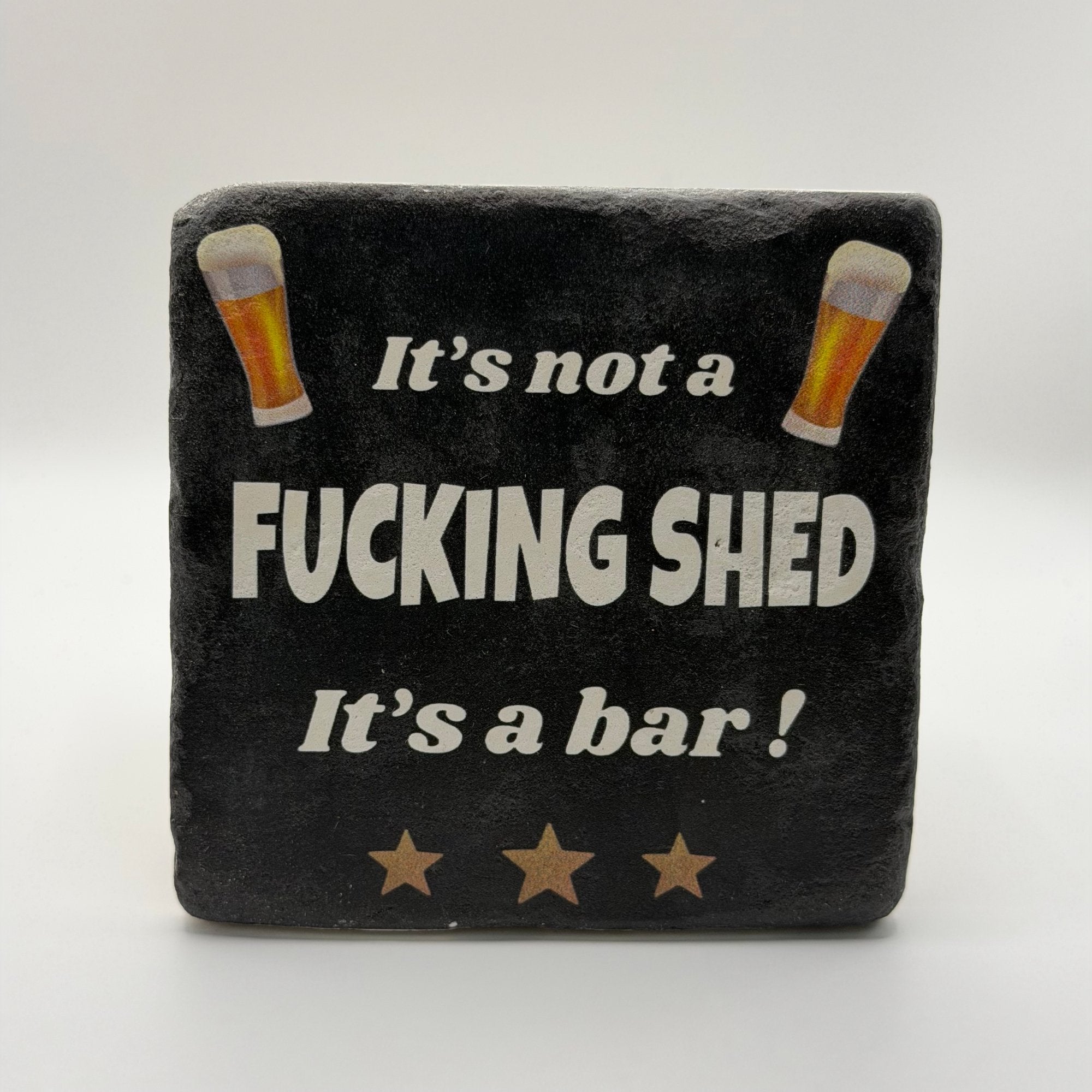 Funny quote 'It's Not a Fucking Shed It's a Bar' printed on square travertine stone coaster