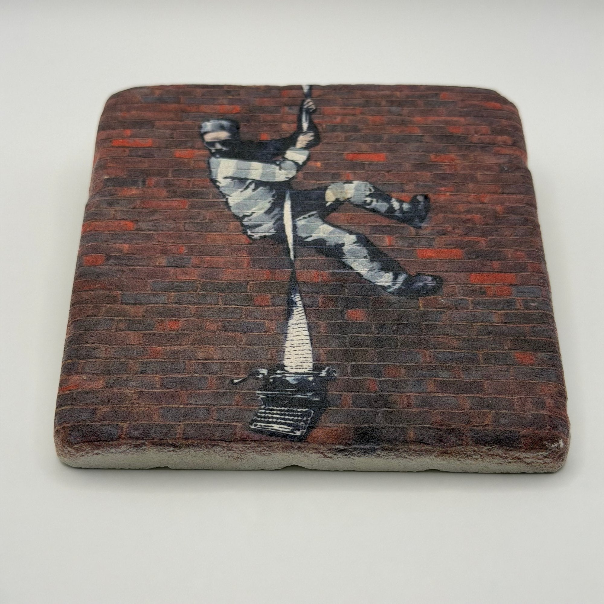 Banksy's Create Escape artwork printed on square travertine stone coaster