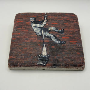Banksy's Create Escape artwork printed on square travertine stone coaster